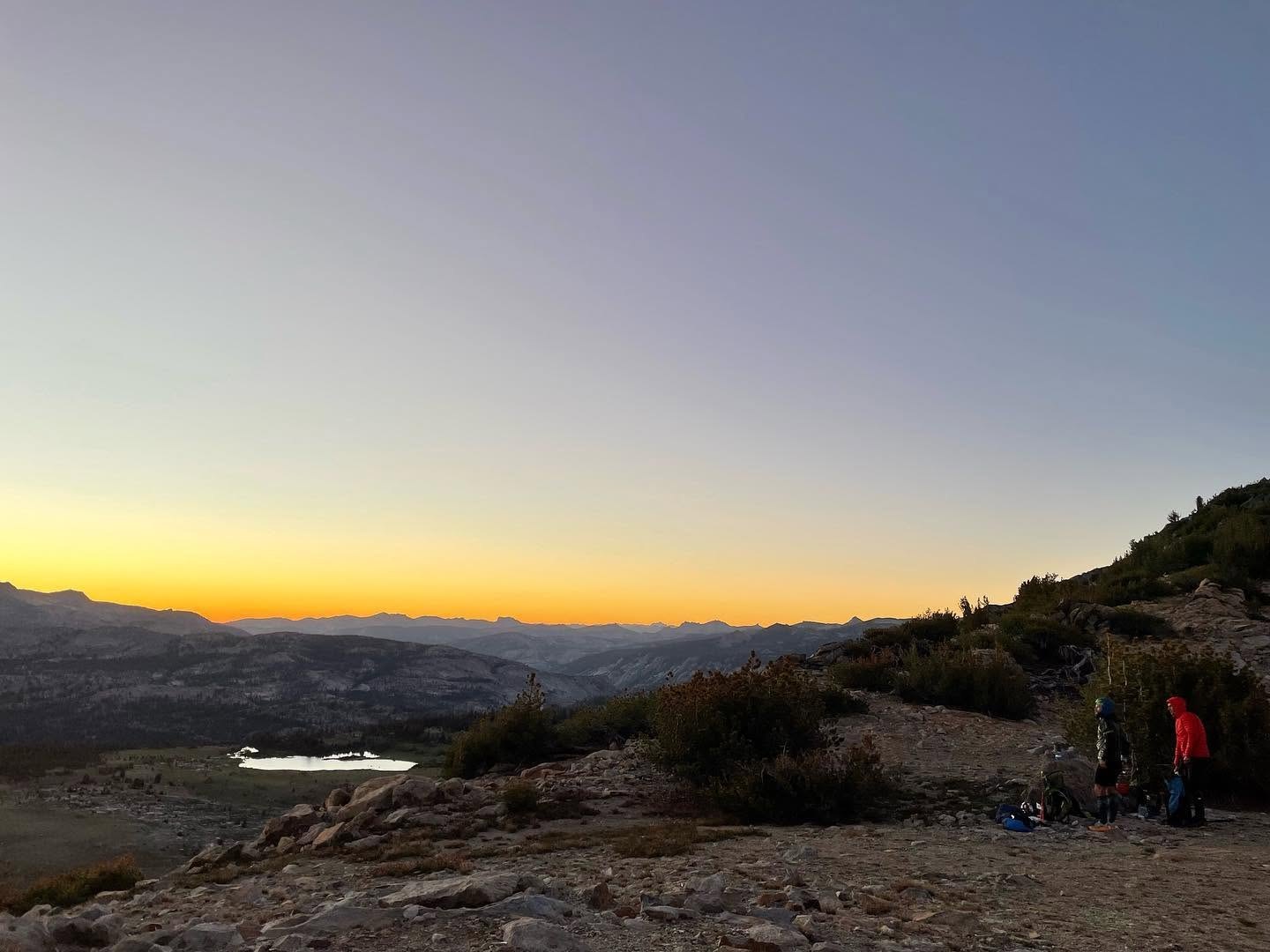 Two members of the Convoluted Bliss team sort gear on a granite bench above a lake at dusk just before camp