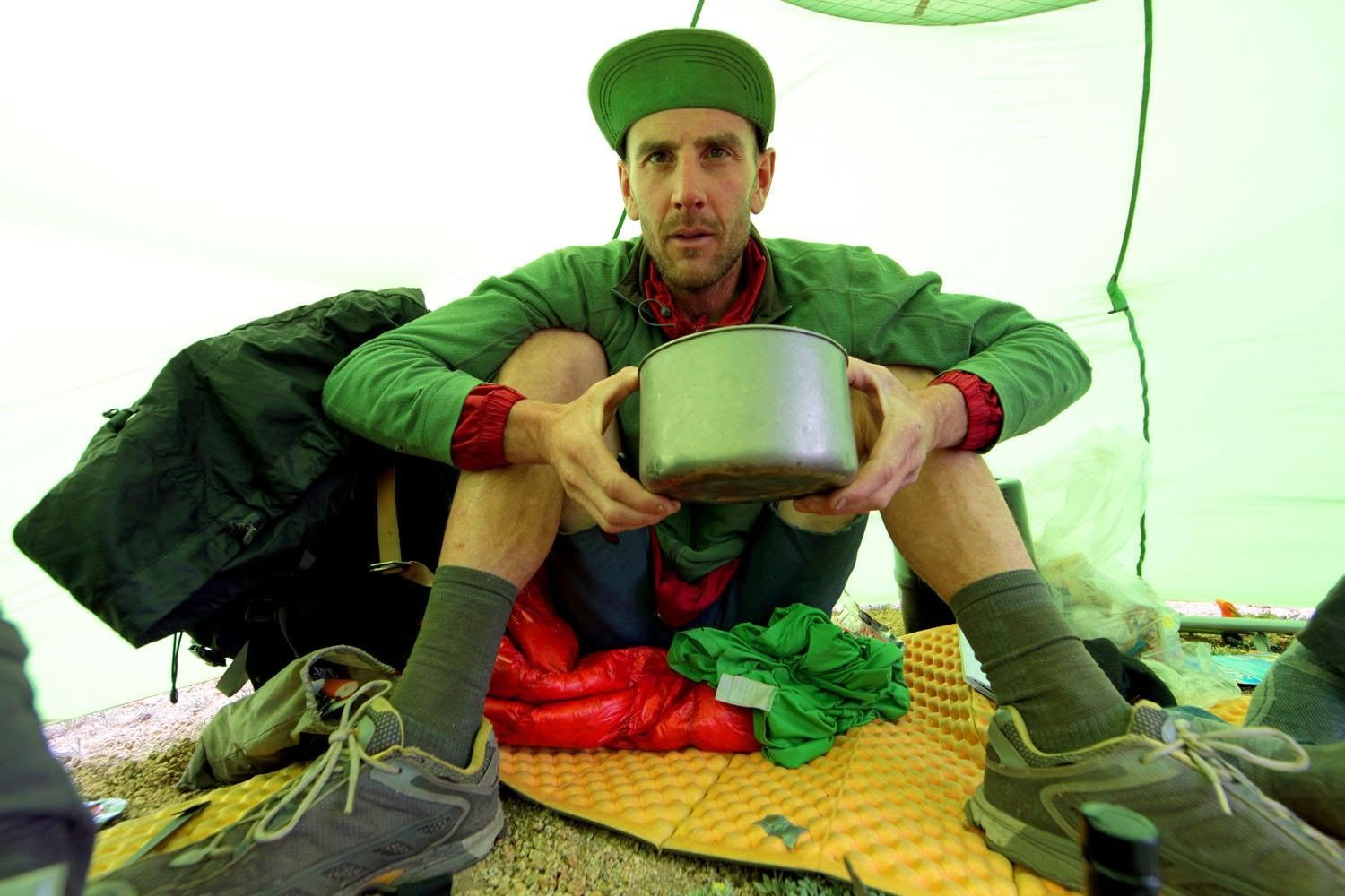 Jason Lakey sits inside a lightweight tent holding a cooking pot