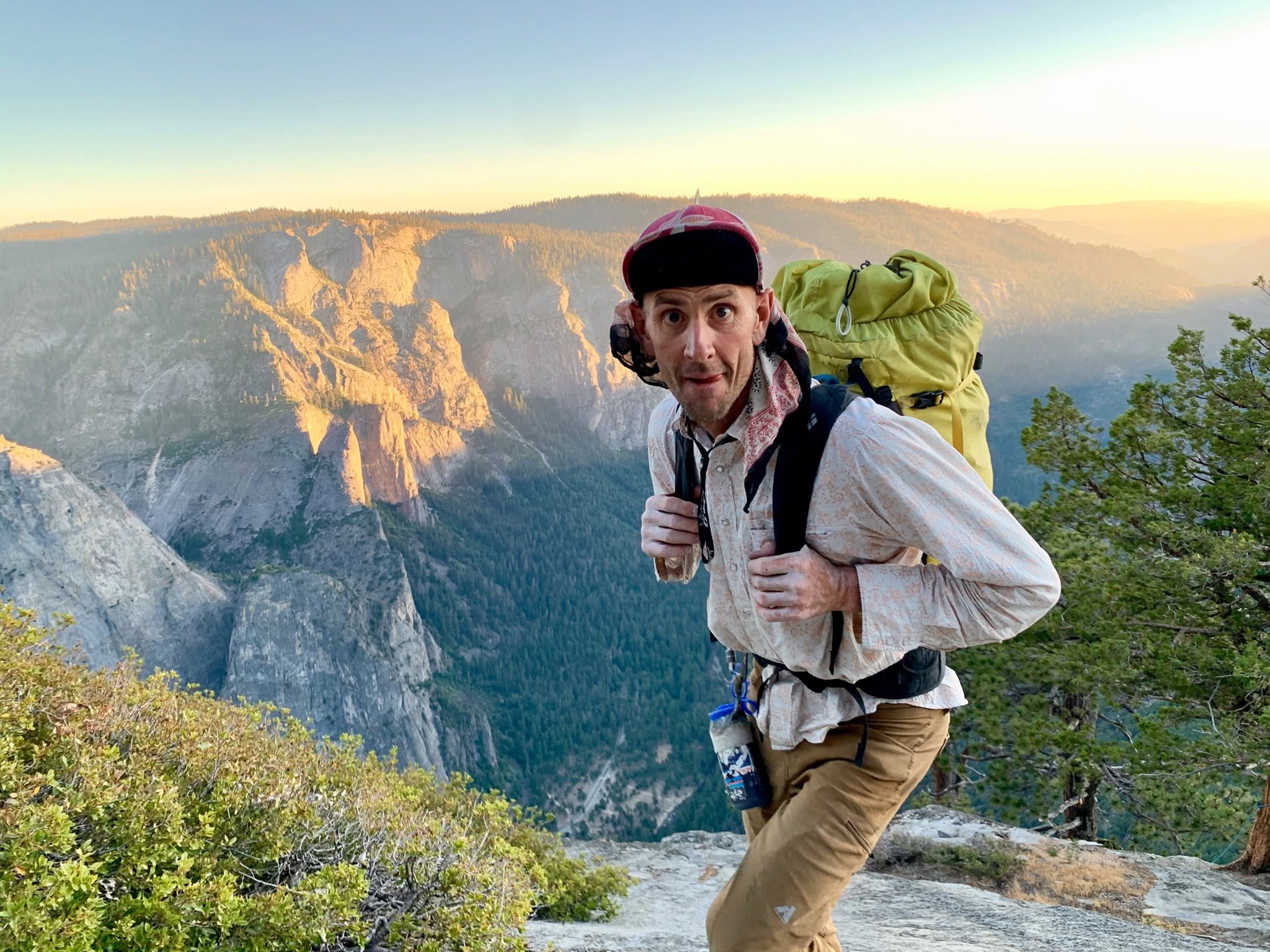 Jason Lakey carries a large yellow pack above Yosemite Valley at golden hour, with North Dome behind him
