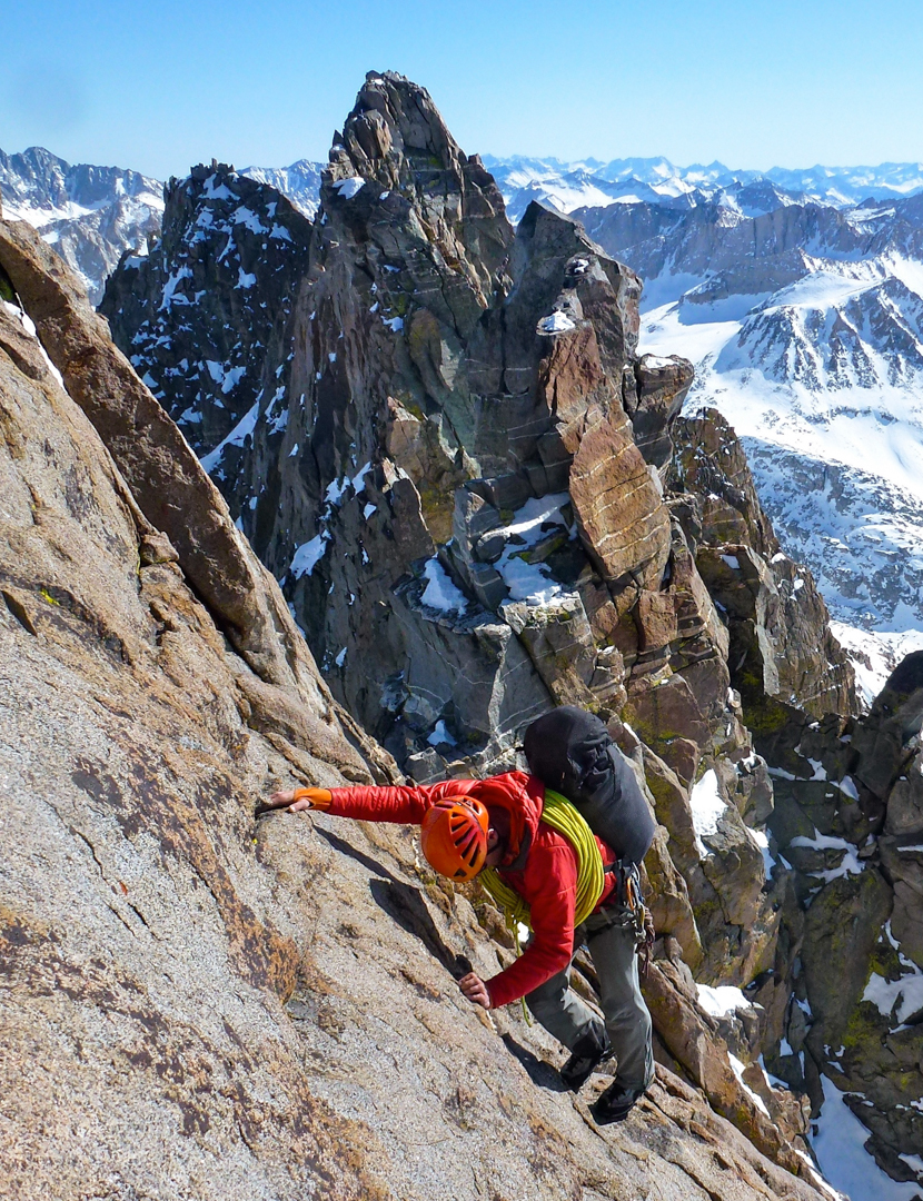 Jed Porter in a red jacket and orange helmet climbing exposed granite above the snowy Palisades