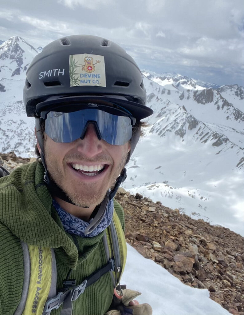 Matt Zupan smiles in a climbing helmet on a snowy Sierra summit
