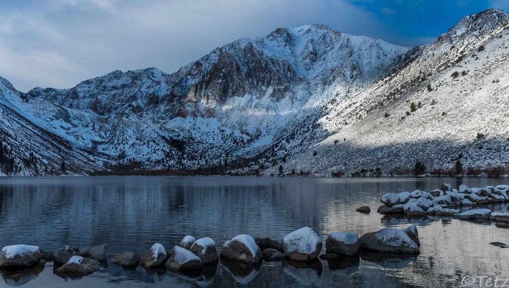 Snow-covered Mount Laurel rises above Convict Lake under broken clouds