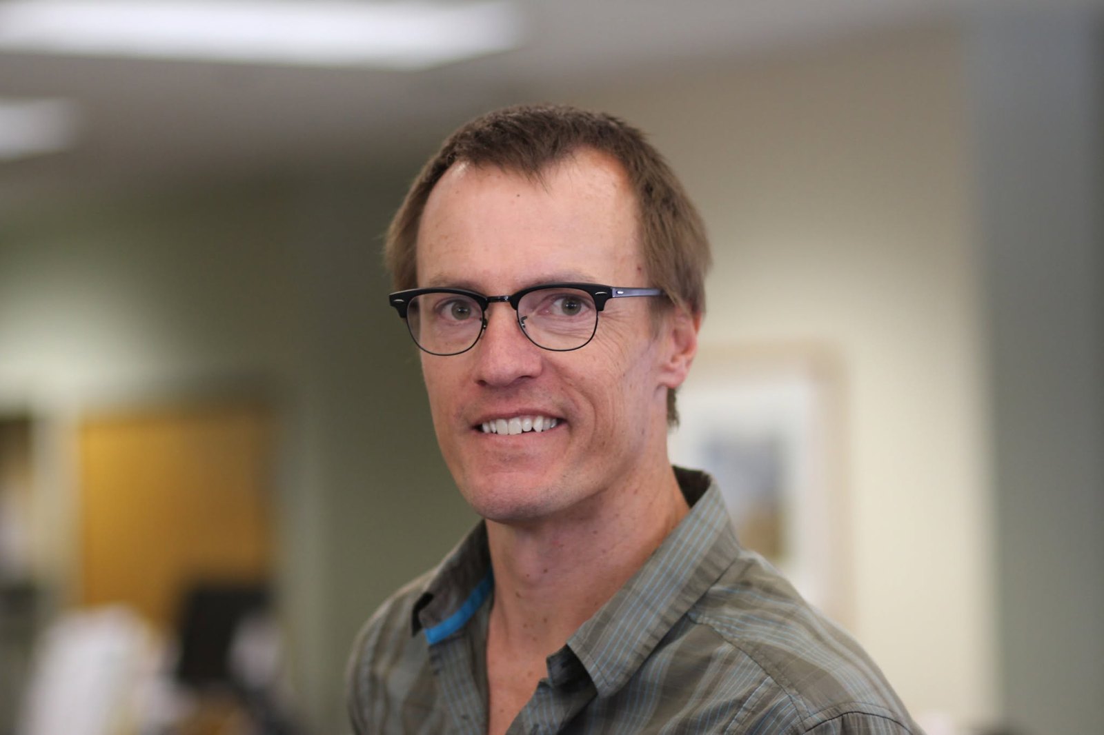 Peter Clark smiles for a head-and-shoulders portrait while wearing dark-framed glasses