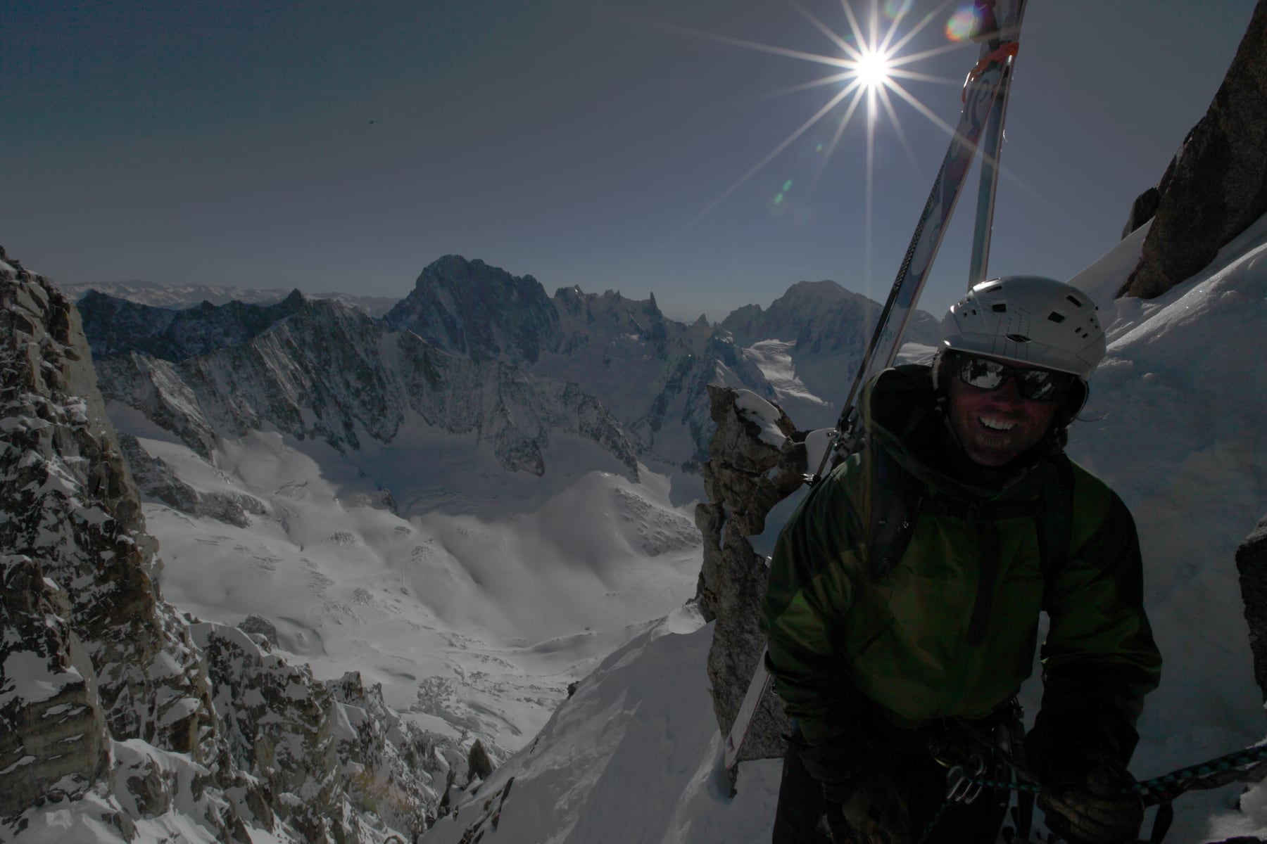 Ryan Boyer smiles with skis on his pack at a snowy alpine col above the Argentière basin
