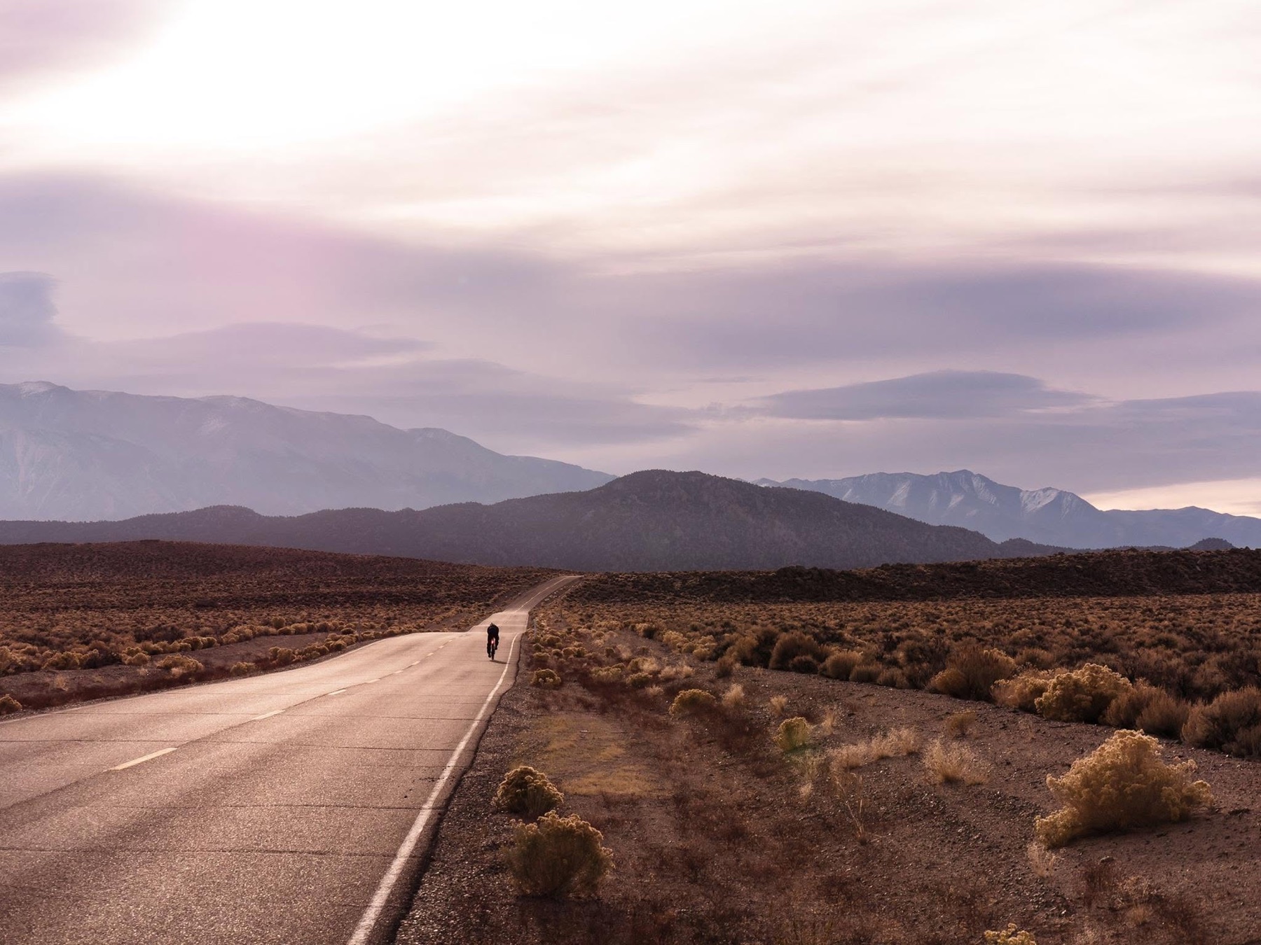 A lone cyclist follows a high-desert road toward the eastern Sierra beneath a wide evening sky