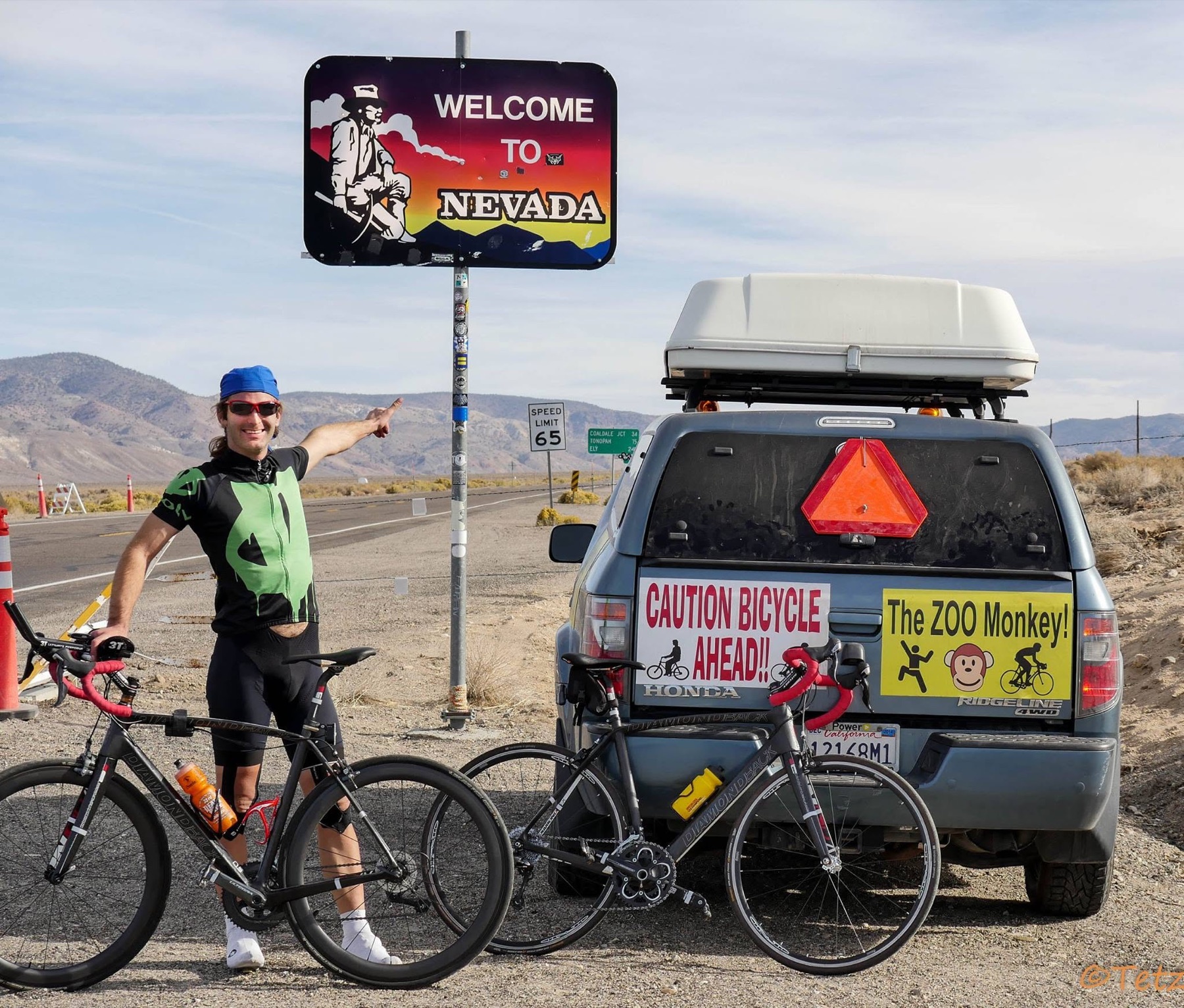 A cyclist stands with a road bicycle beneath the Welcome to Nevada sign at the eastern end of the 2014 Trans-California Crossing Direct